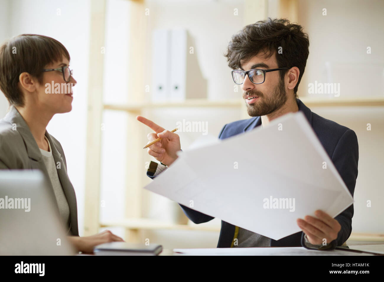 L'équipe d'affaires au travail : deux collègues collaborant au projet, creative man holding documents et doigt de parler avec enthousiasme à femme Banque D'Images