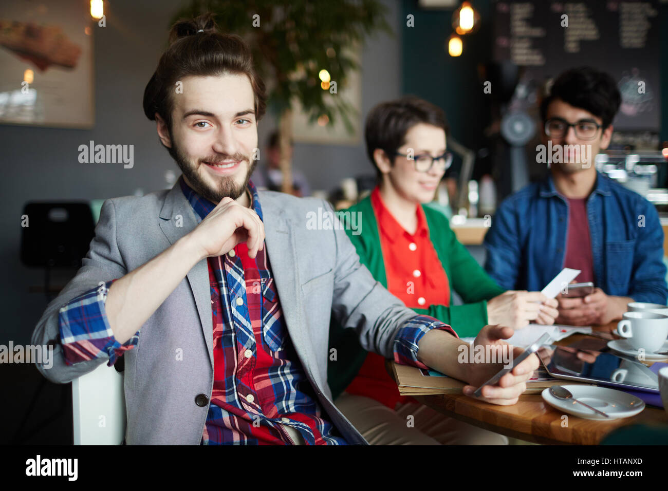 Portrait de trois personnes créatives habillés en tenue d'affaires décontractée à table dans un café, se concentrer sur les jeunes smiling businessman with long hair smiling gaiement lo Banque D'Images