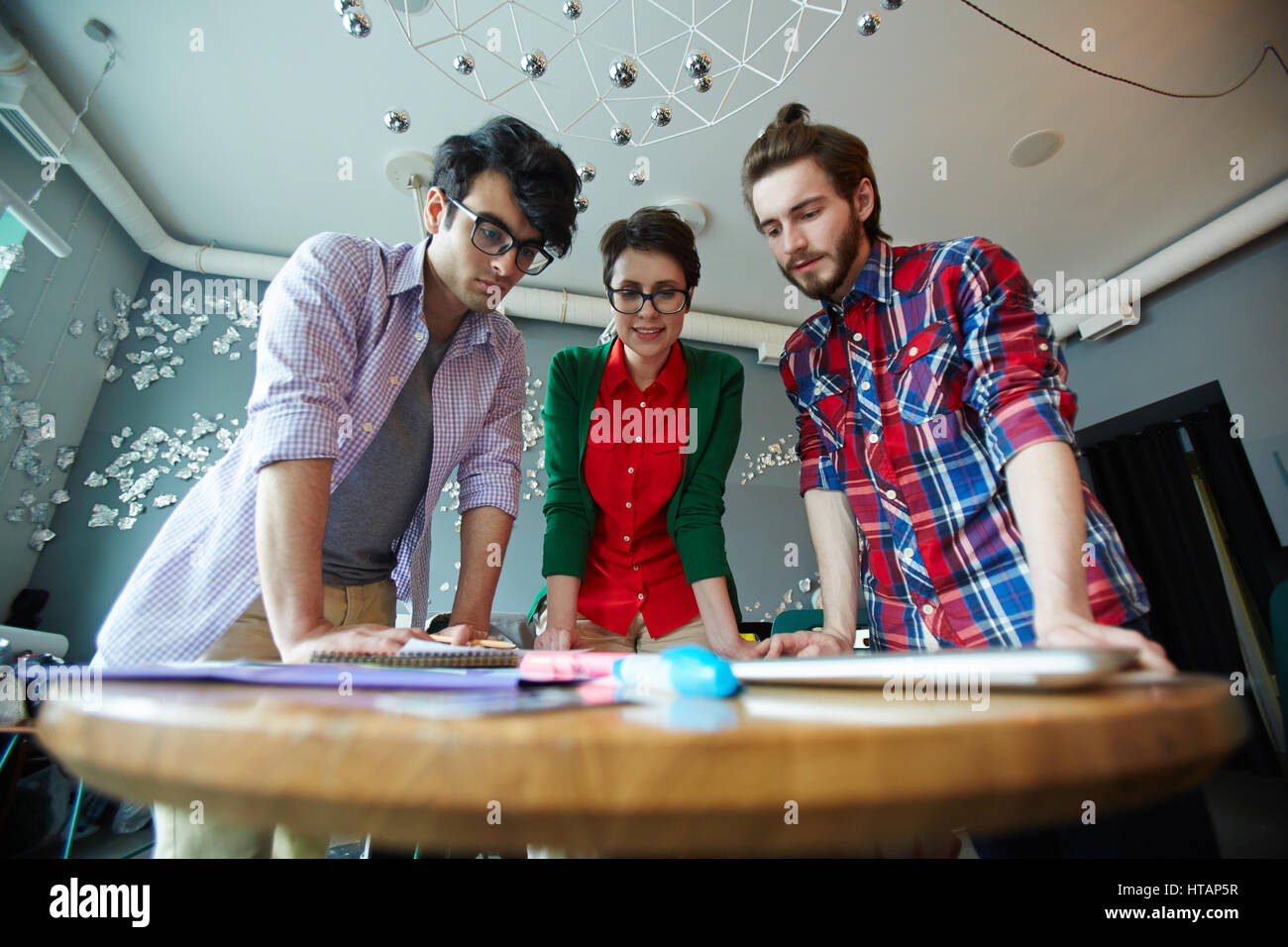 Low angle shot de l'équipe de jeunes gens créatifs portant les tenues de collaborer à la réunion dans un bureau moderne et d'une petite table ronde permanente lookin Banque D'Images
