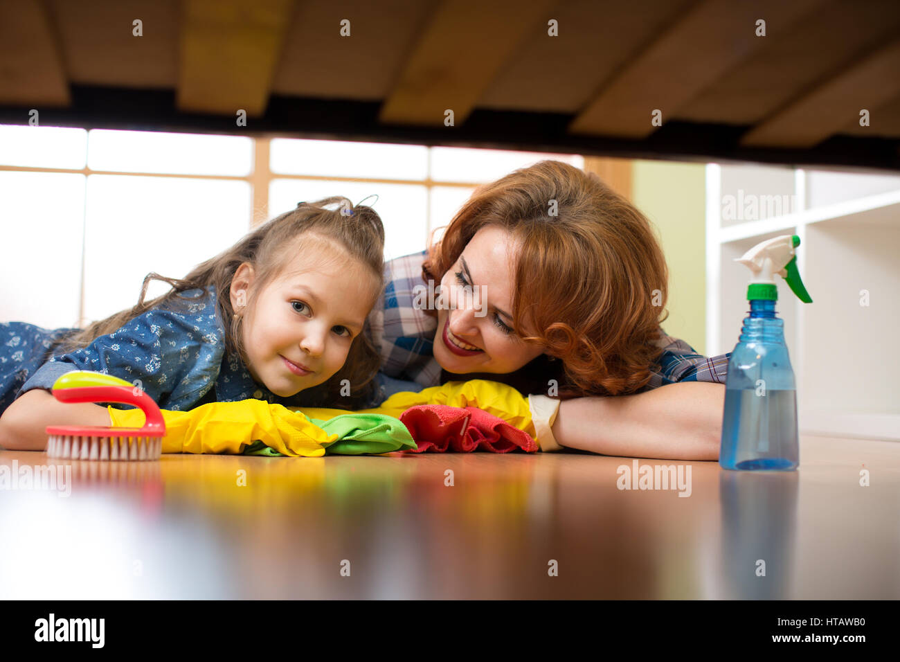 Smiling family mère et enfant fille chambre propre à la maison. Femme d'âge moyen et de l'enfant fille essuya marbre sous lit Banque D'Images