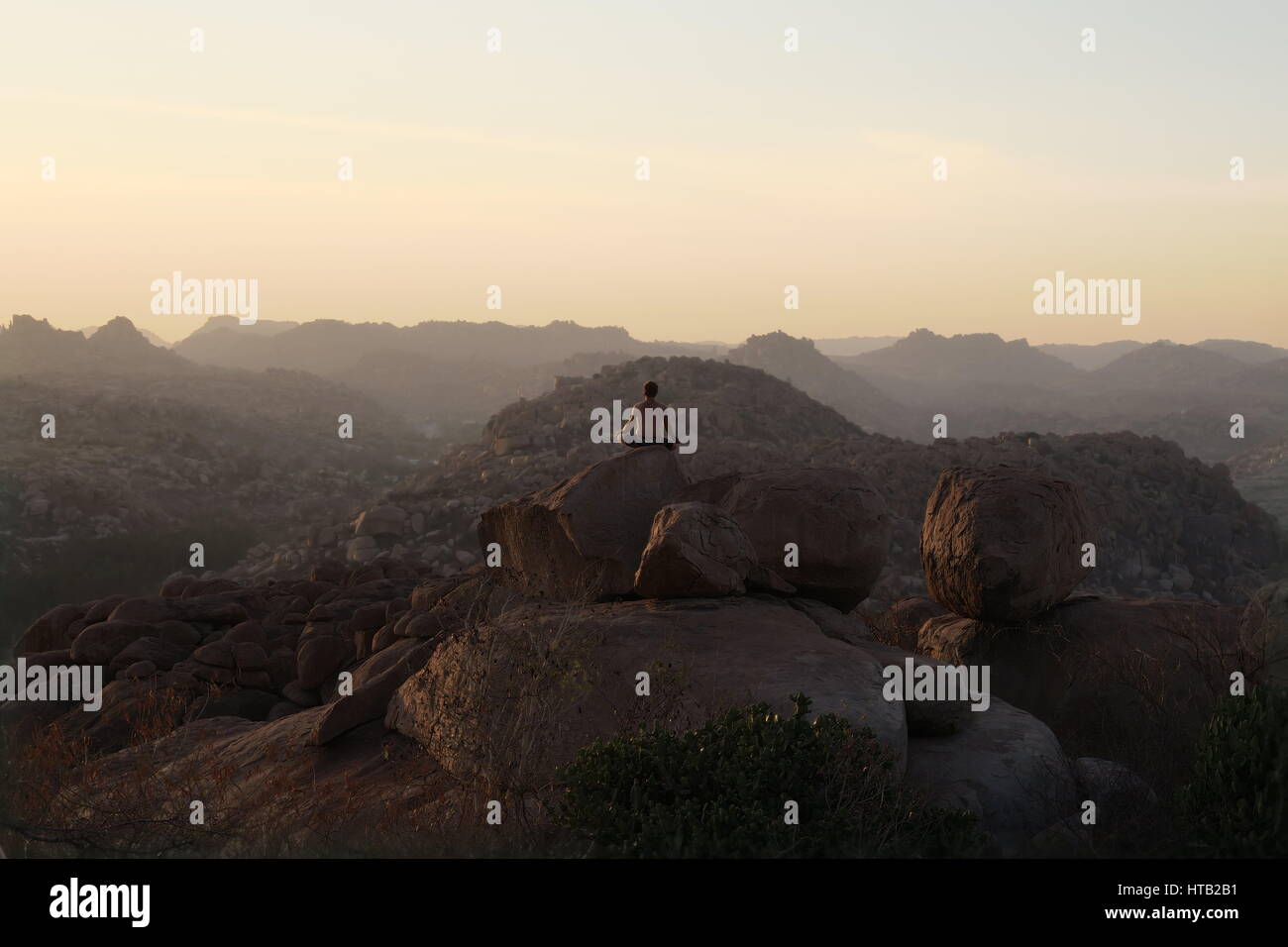 Guy méditant sur un rocher au-dessus du singe temple à Hampi, quelques instants avant le coucher du soleil. Banque D'Images
