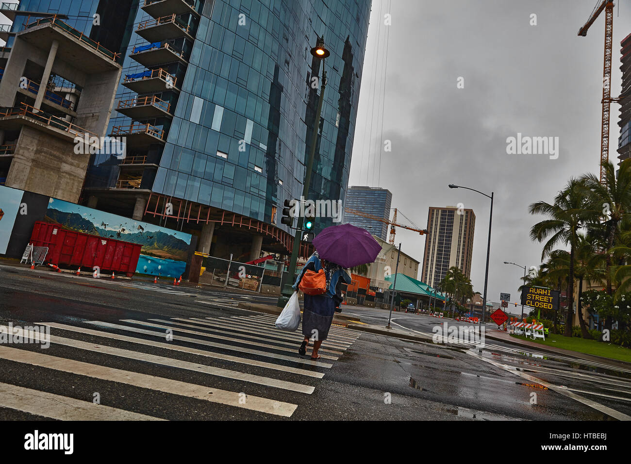 Honolulu, Hawaii, USA - 7 août ; 2016 : une femme non identifiée avec parapluie crossing street dans la pluie sous un ciel orageux à Honolulu, Oahu, Hawaii. Banque D'Images