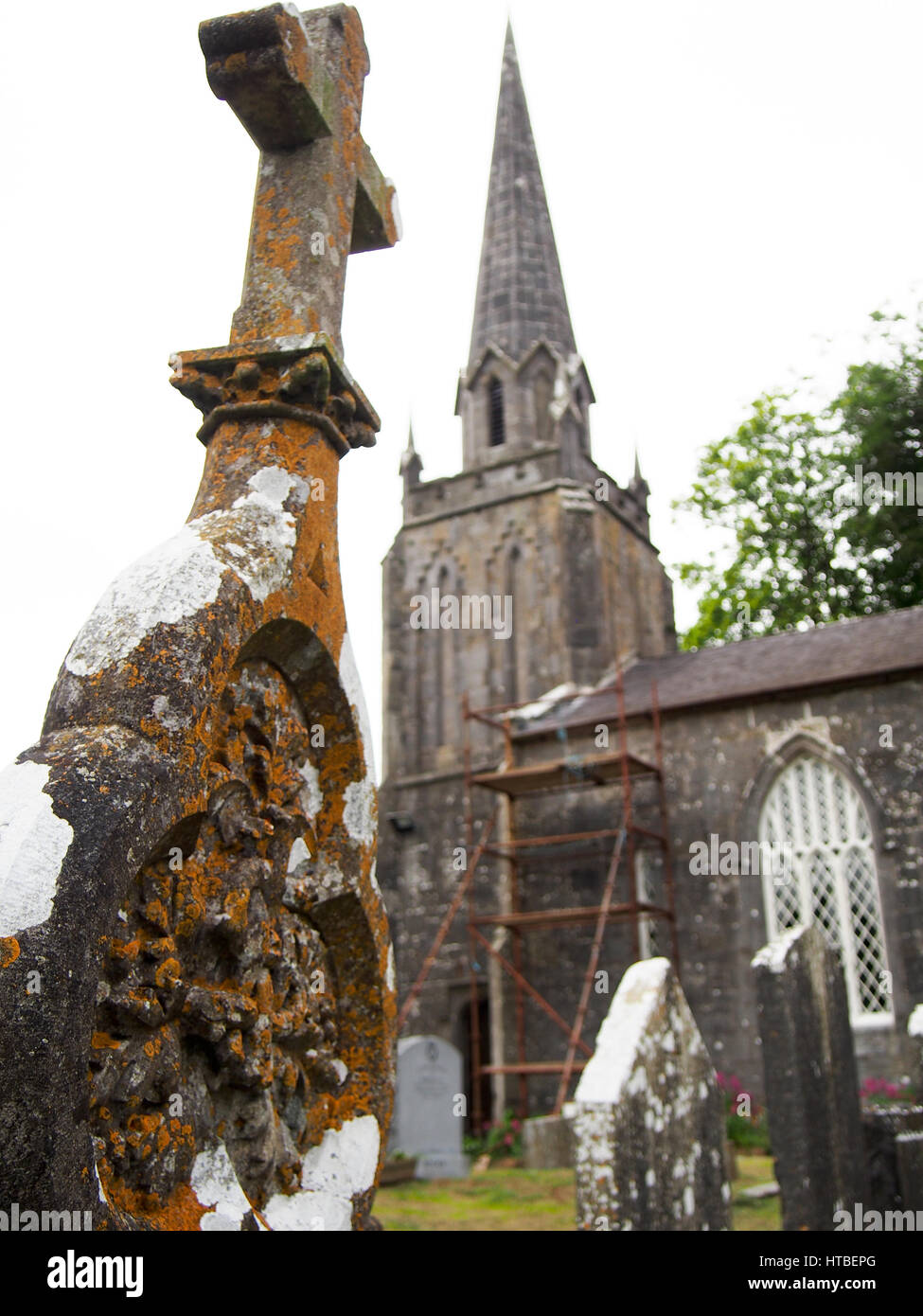 Détail d'un old weathered pierre tombale avec une église catholique rural dans l'arrière-plan dans le comté de Cork, Irlande. Banque D'Images