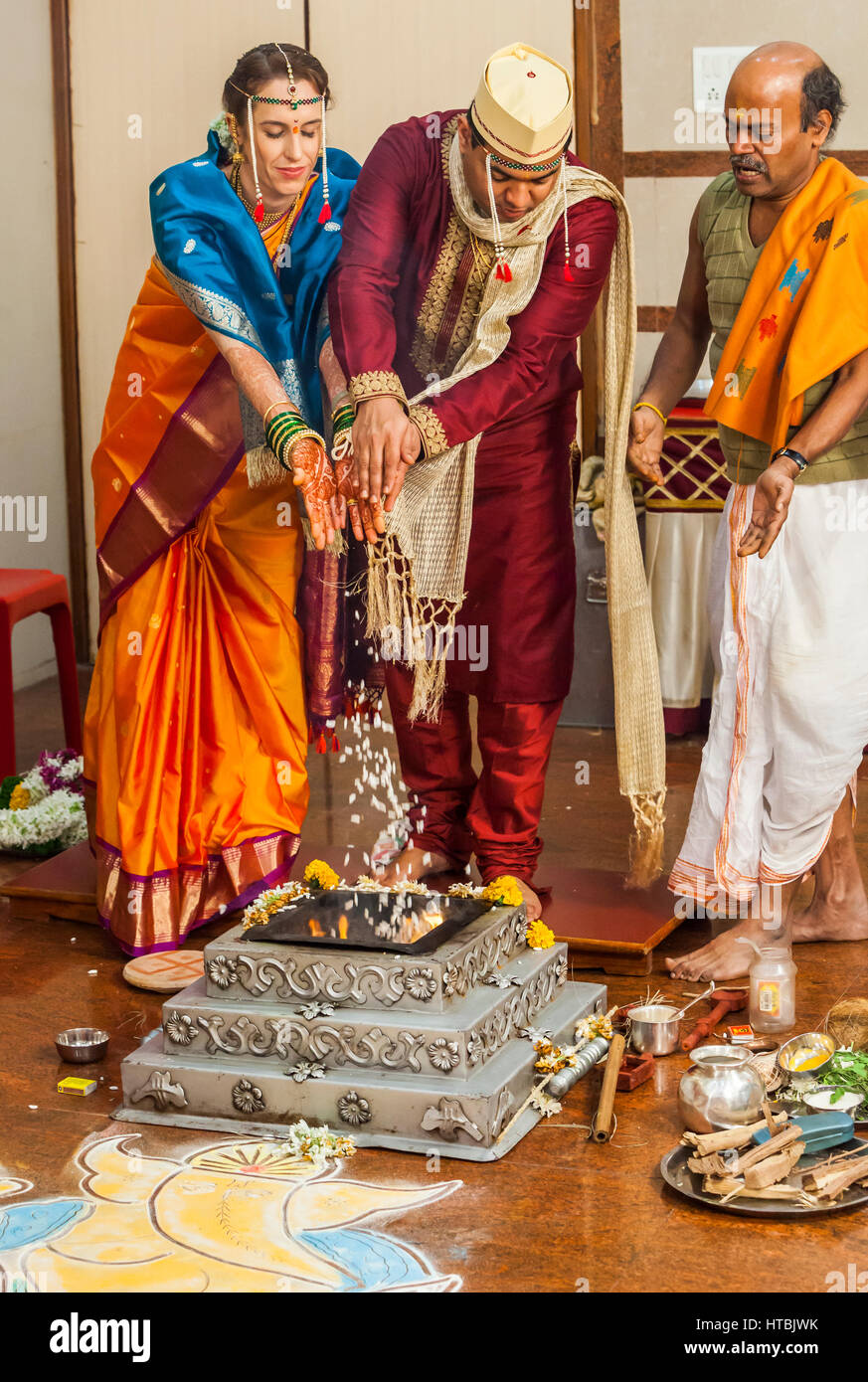 La mariée et le marié à un mariage indien en faisant des offrandes de riz soufflé à la Holy Fire accompagné par le prêtre. Banque D'Images