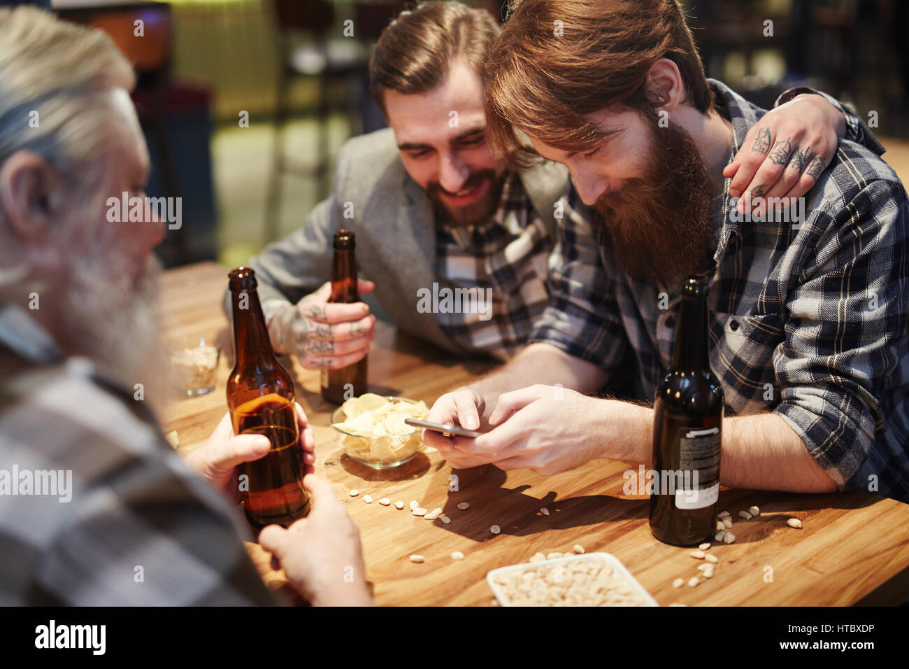 Trois hommes barbus avec des bouteilles de bière, passer du temps dans un pub Banque D'Images