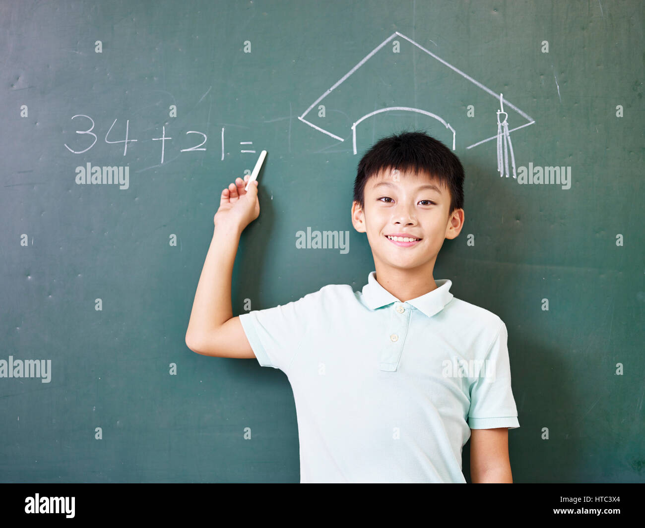 L'école primaire asiatique garçon debout sous un chapeau de doctorat dessiné avec la craie sur tableau noir. Banque D'Images