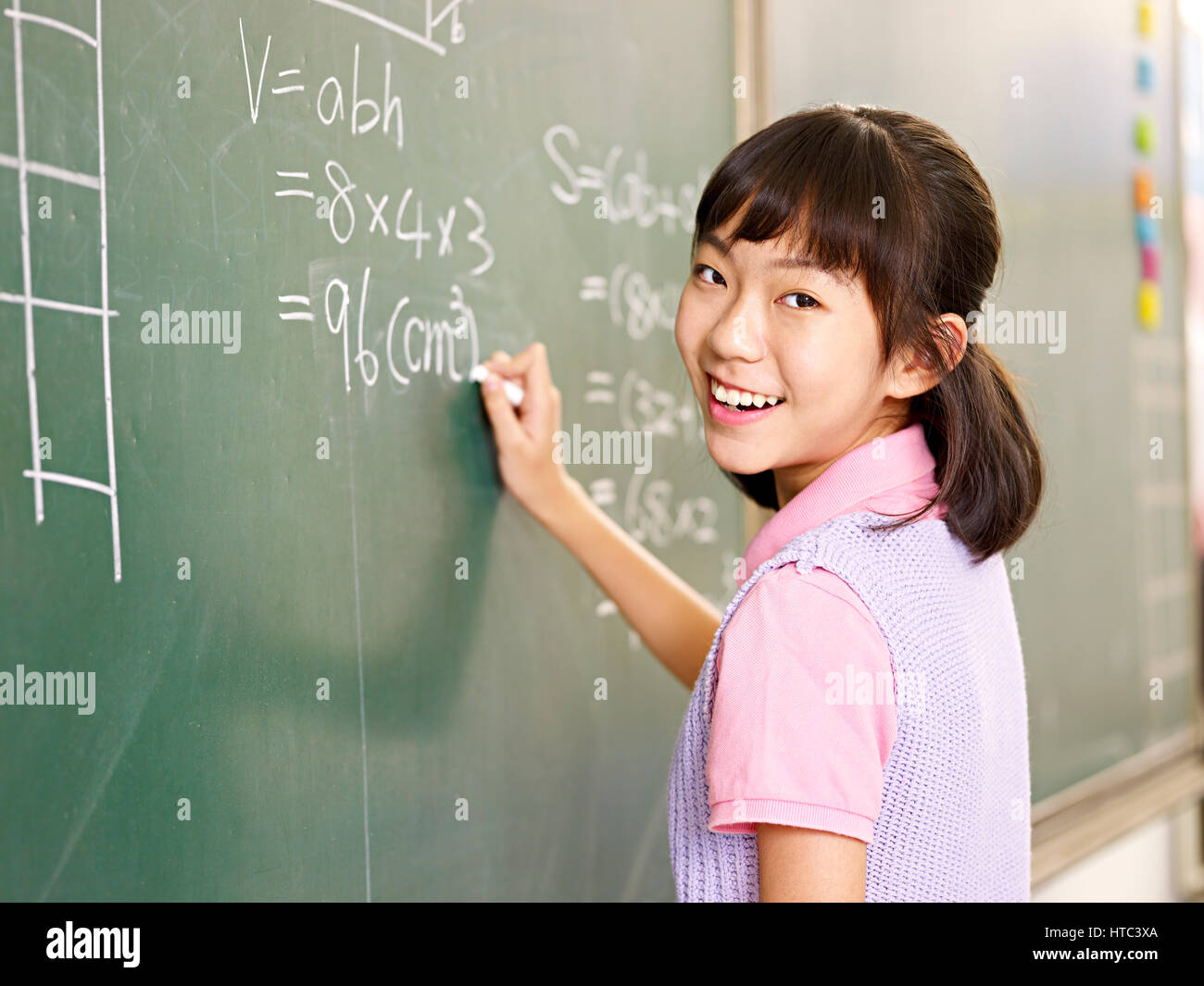 Écolière élémentaire asiatique à la caméra tout en souriant à résoudre un problème mathématique. Banque D'Images