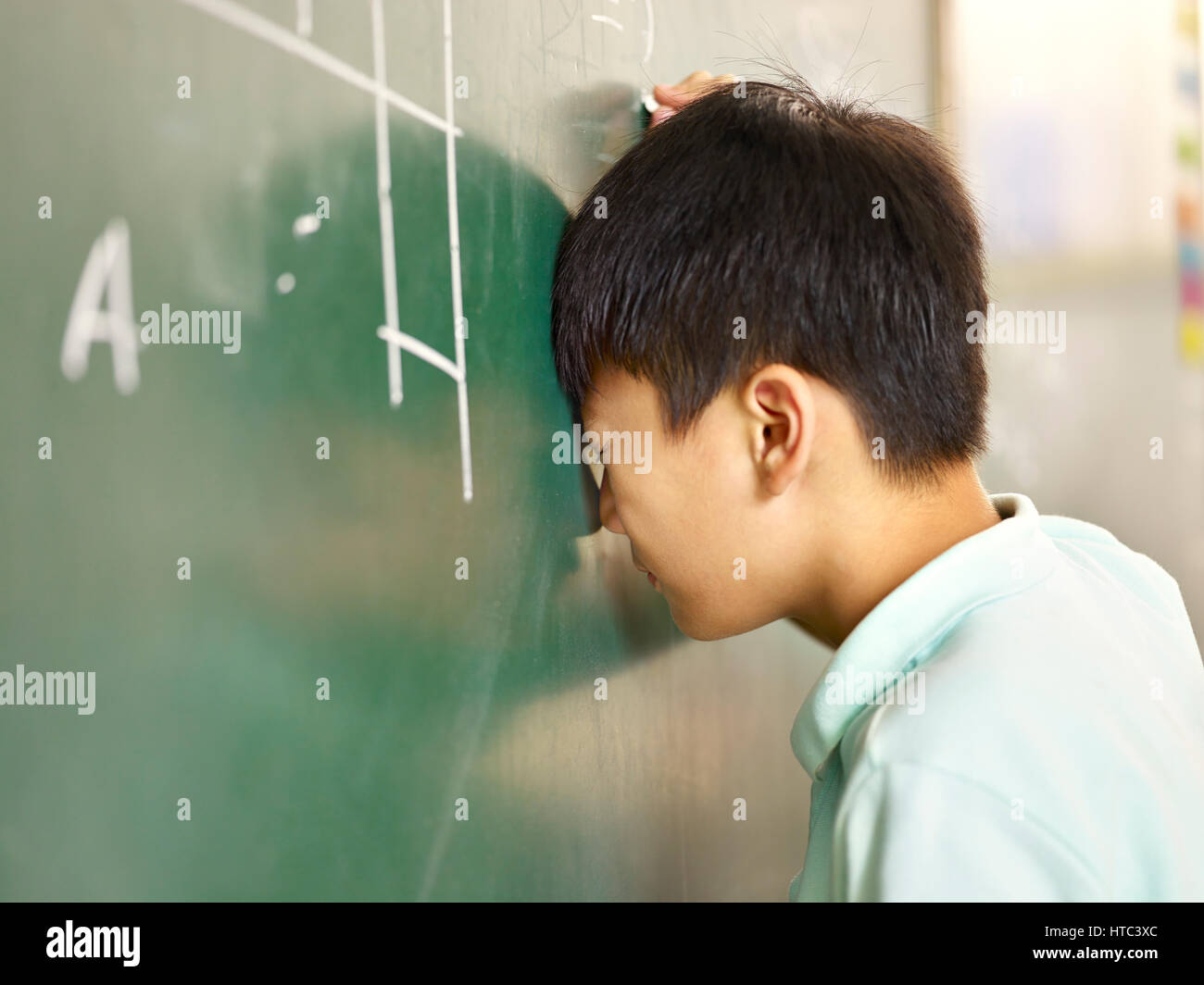 Asiatique douloureux écolier élémentaire frappant sa tête sur tableau noir alors que la résolution de problème de géométrie. Banque D'Images
