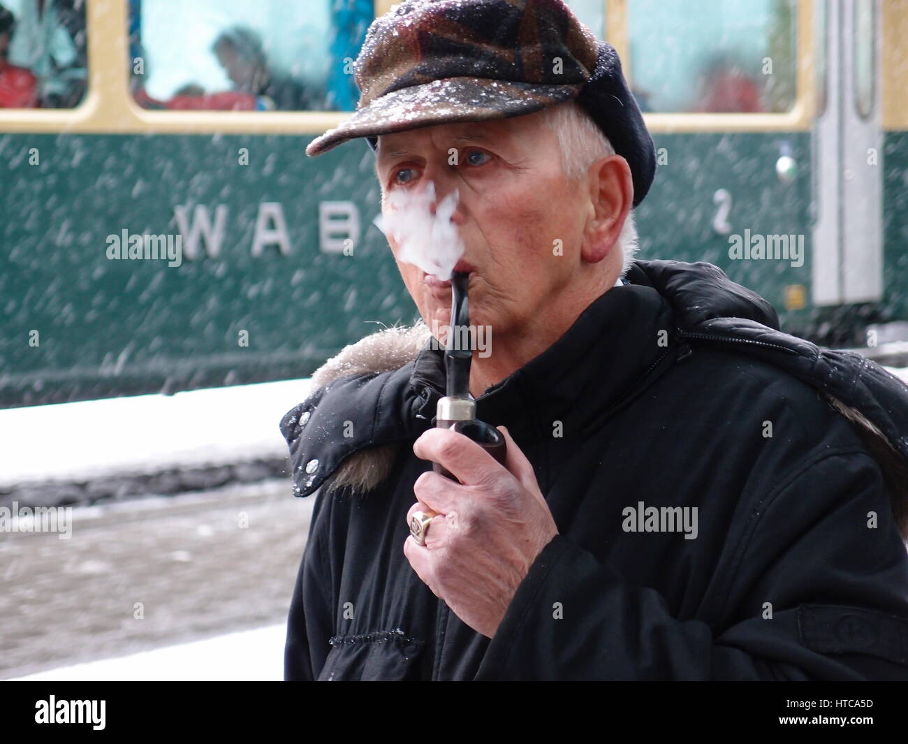 Vieil homme fumant une pipe dans la neige à la gare de Wengen en Suisse.  Wengernalpbahn (WAB) un train est à l'arrière-plan Photo Stock - Alamy