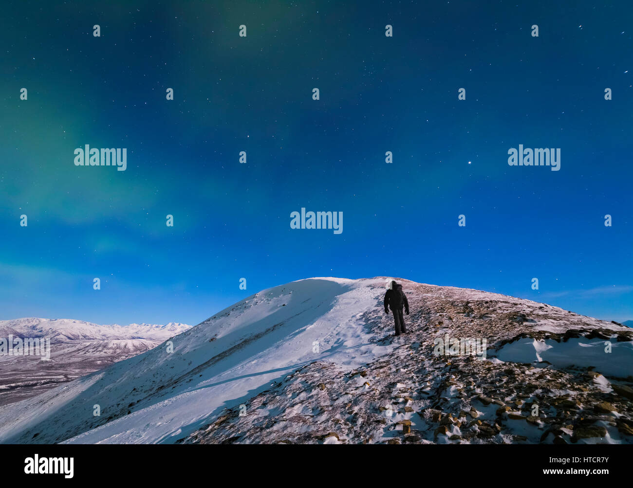 Un homme monte au haut de Donnelly Dome (près de Delta Junction) sur une nuit de pleine lune dans des températures sous zéro pour photographier les aurores boréales. Banque D'Images