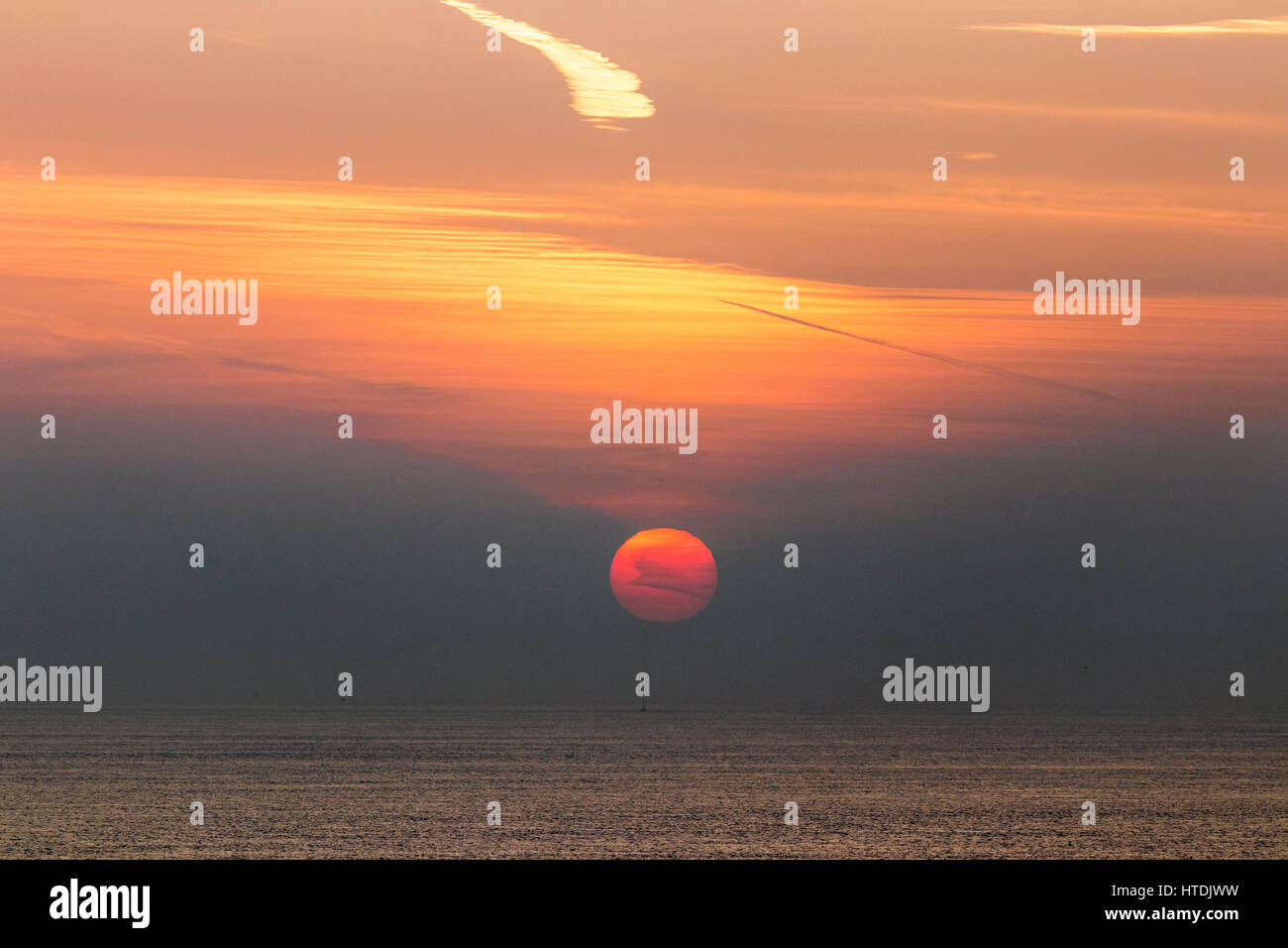 Le lever du soleil sur la mer, Manche, avec le soleil une boule orange à moitié caché par la brume atmosphérique Banque D'Images
