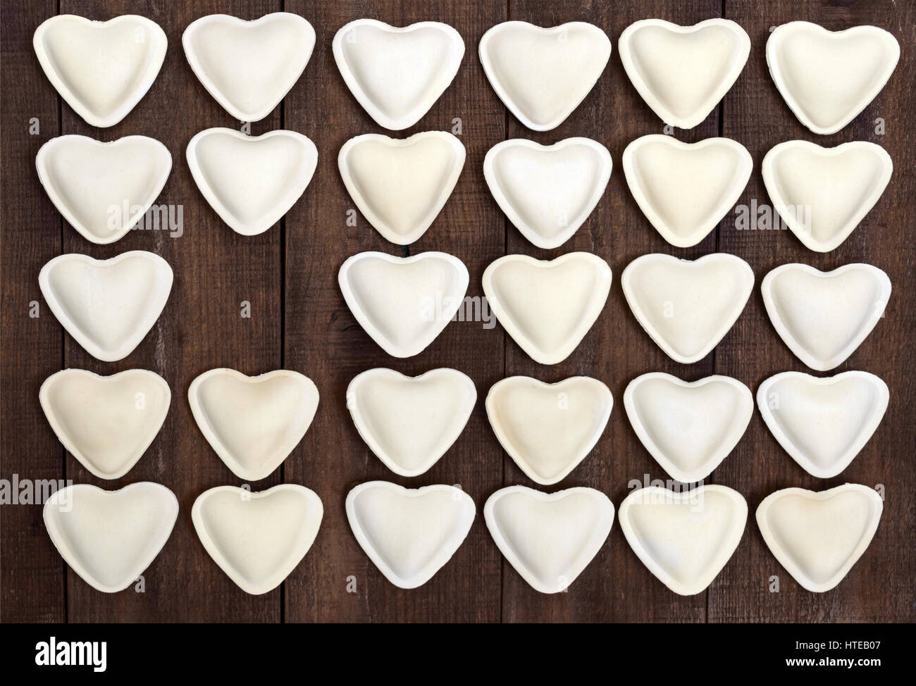 Pâte non cuite en forme de cœur (boulettes, ravioli, pelmeni), disposés en rangées sur un fond de bois sombre. Banque D'Images