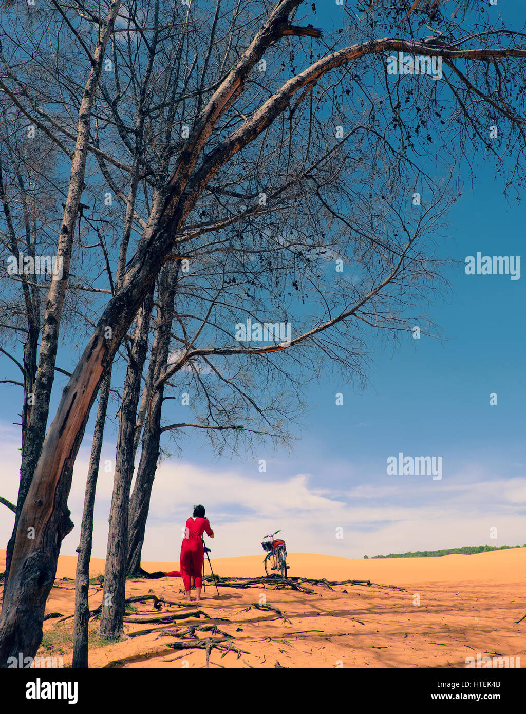 Femme voyageant seule à Mui Ne, Vietnam, jeune fille en robe rouge et jaune avec des selfies vélo sur la colline de sable en vertu de l'arbre, bon voyage touristique en summetime Banque D'Images