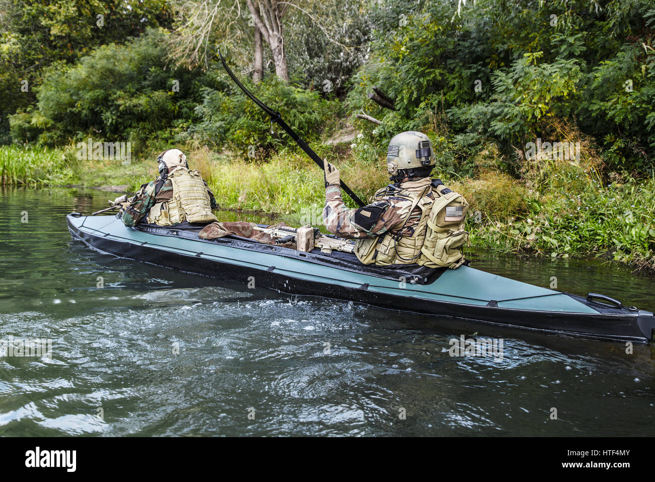 Les hommes des forces spéciales avec des visages peints en tenue de camouflage de l'armée de pagaie en kayak. Bateau de l'autre côté de la rivière, la mission de diversion, vue arrière Banque D'Images Les hommes des forces spéciales avec des visages peints en tenue de camouflage de l'armée de pagaie en kayak. Bateau de l'autre côté de la rivière, la mission de diversion, vue arrière Banque D'Images