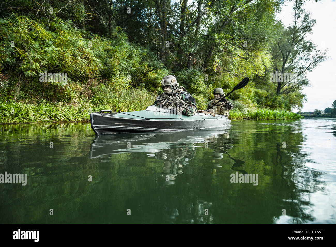 Les hommes des forces spéciales avec des visages peints en tenue de camouflage de l'armée de pagaie en kayak. Déménagement en bateau sur la rivière, vue sur la diagonale, la mission de diversion Banque D'Images Les hommes des forces spéciales avec des visages peints en tenue de camouflage de l'armée de pagaie en kayak. Déménagement en bateau sur la rivière, vue sur la diagonale, la mission de diversion Banque D'Images