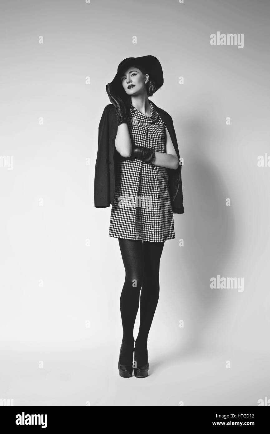 Belle jeune femme avec des lèvres rouge maquillage en retro noir et blanc robe, chapeau, veste et gants de cuir debout sur fond gris. Monochrome. Co Banque D'Images