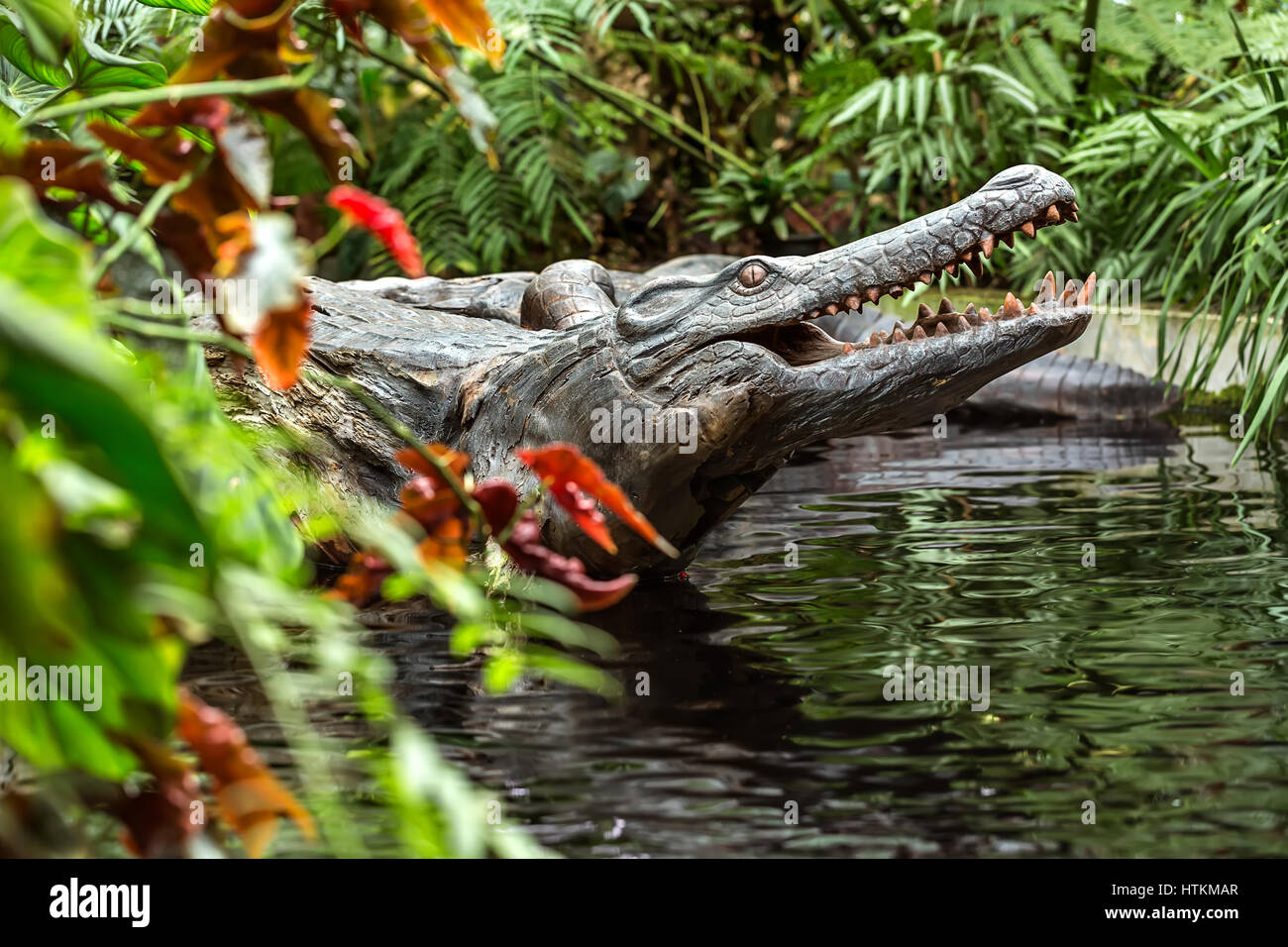 Crocodile en bois sculpture dans l'étang dans la forêt de nuages à Singapour. Il entouré par les plantes multicolores. Libre. L'horizontale. Banque D'Images
