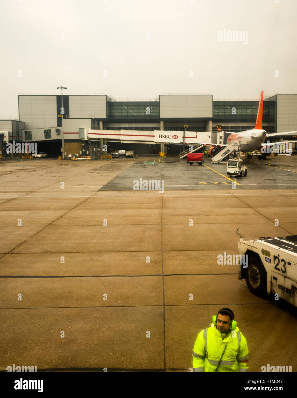 Londres Gatwick. England UK. Les avions d'EasyJet sur la piste de l'aéroport Gatwick de Londres la préparation pour le décollage. Membre de l'équipe au sol sur la piste mouillée portant une veste haute visibilité fluorescent. L'un des bâtiments de l'aéroport est à l'arrière-plan. Banque D'Images
