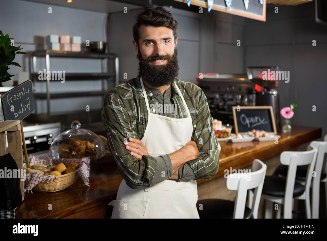 Portrait of smiling le personnel masculin debout avec les bras croisés au compteur dans la région de coffee shop Banque D'Images