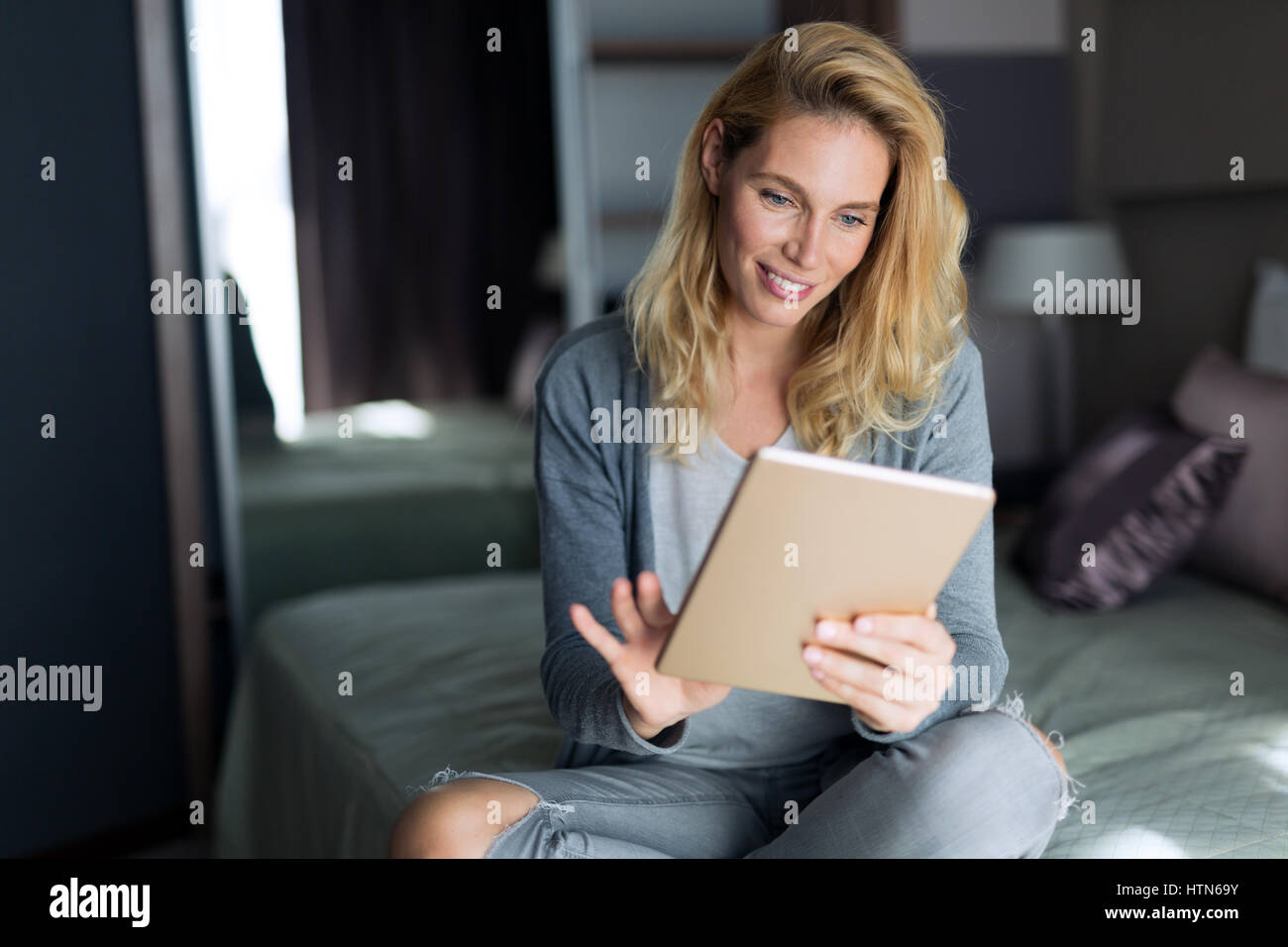 Belle blonde woman relaxing on bed abd using tablet Banque D'Images