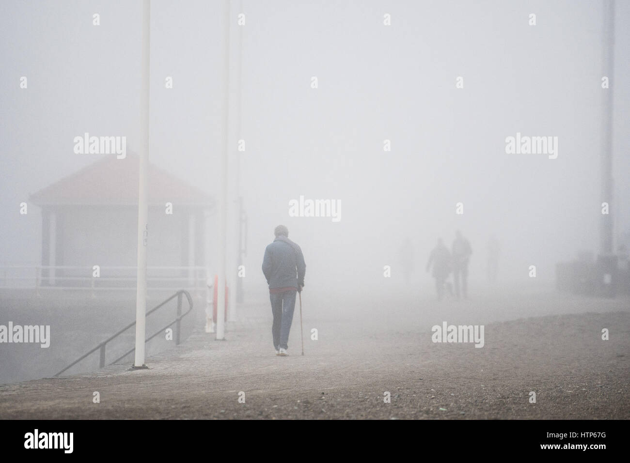 Aberystwyth, Pays de Galles, Royaume-Uni. 14Th Mar, 2017. Météo France : Les gens qui marchent le long de la promenade est obscurci par le brouillard dans la station balnéaire d'Aberystwyth, sur la côte ouest du pays de galles comme un épais manteau gris et froid de la brume de mer tourbillonnant en vient au large de la mer d'Irlande, cet après-midi. Crédit photo : Keith Morris/Alamy Live News Banque D'Images