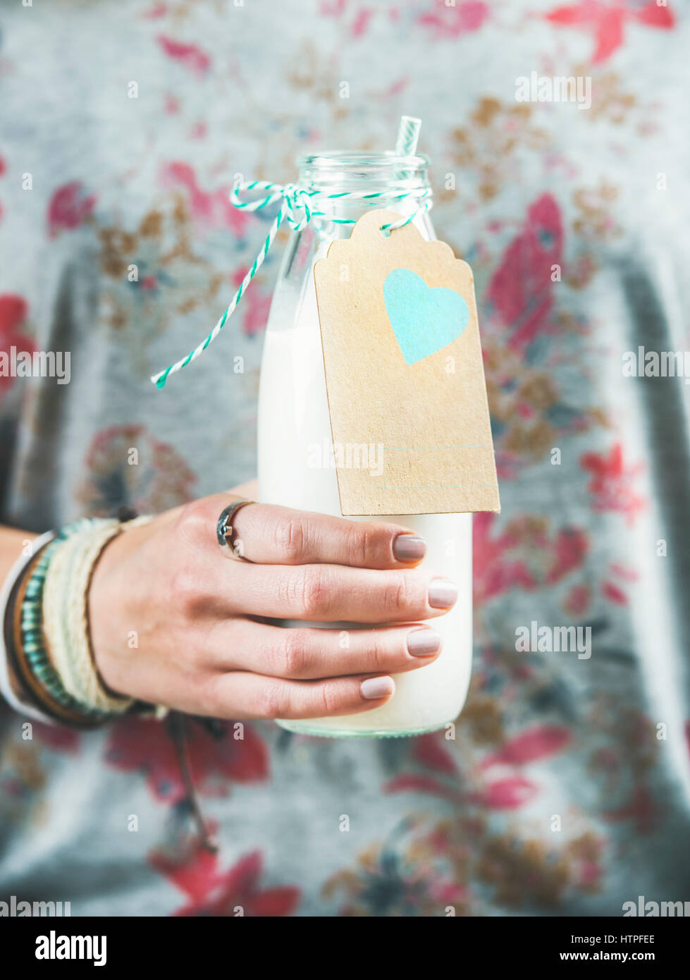 Jeune femme en t-shirt gris avec motif floral holding bouteille de lait d'amande sans produits laitiers dans sa main. Nettoyer, de l'alimentation, les régimes végétaliens, végétariens, santé Banque D'Images