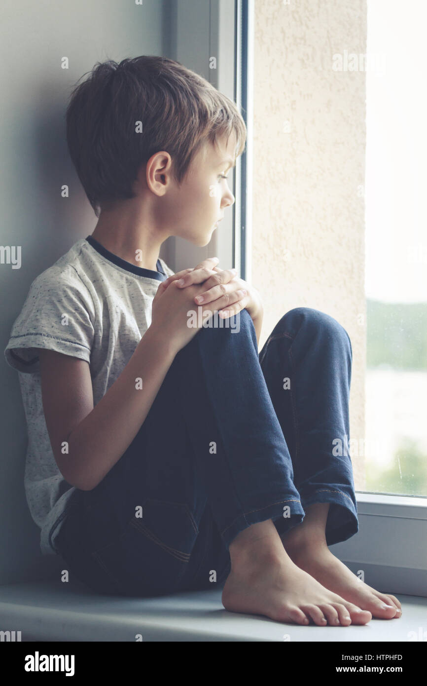 une petit enfant regards en dehors le la fenêtre. le enfant avec une jouet  est assis sur une fenêtre seuil. 22047158 Photo de stock chez Vecteezy