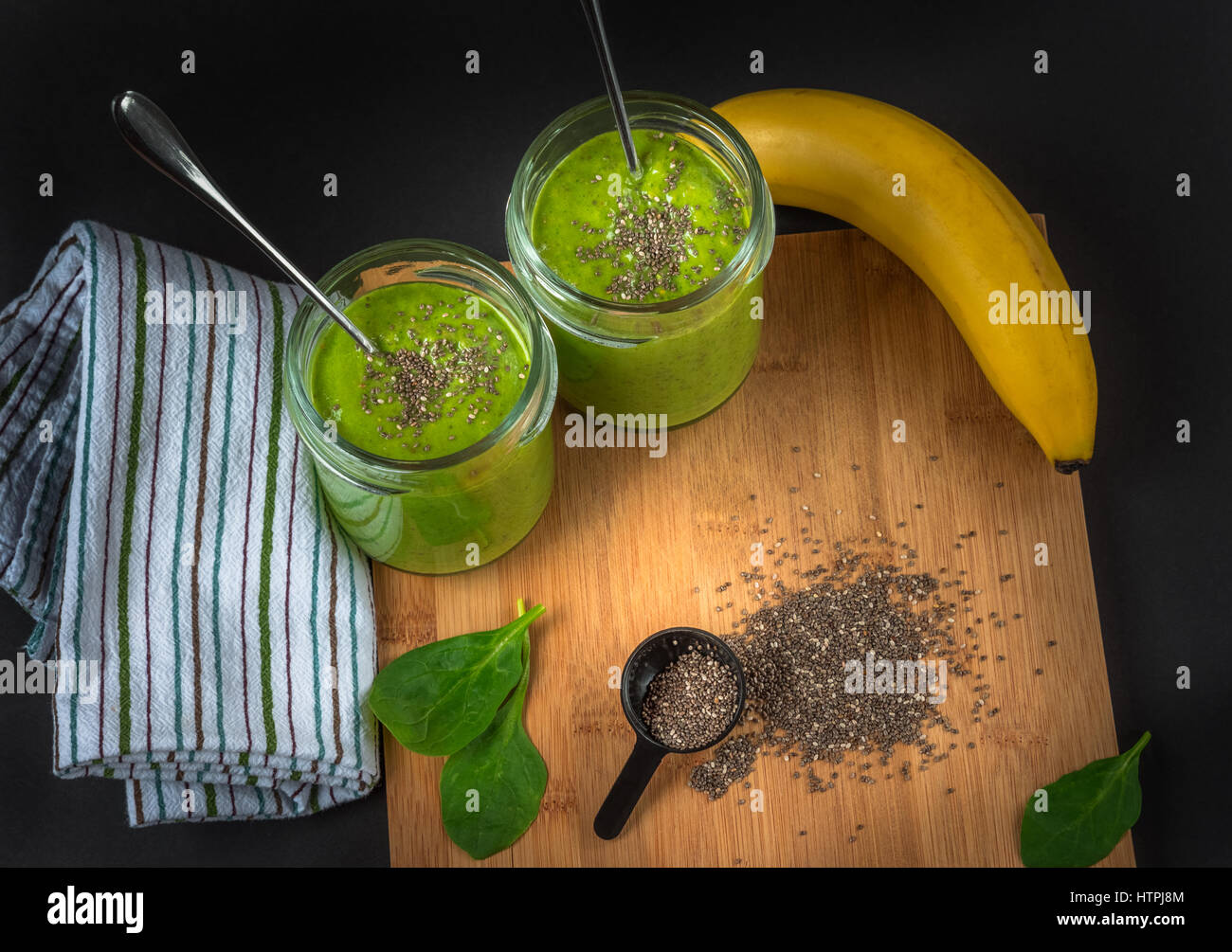 Épinards vert, semences chia, banane et de protéines en poudre dans deux bocaux smoothie sur la surface en bois de bambou, serviette en tissu, fond sombre. bain sain Banque D'Images