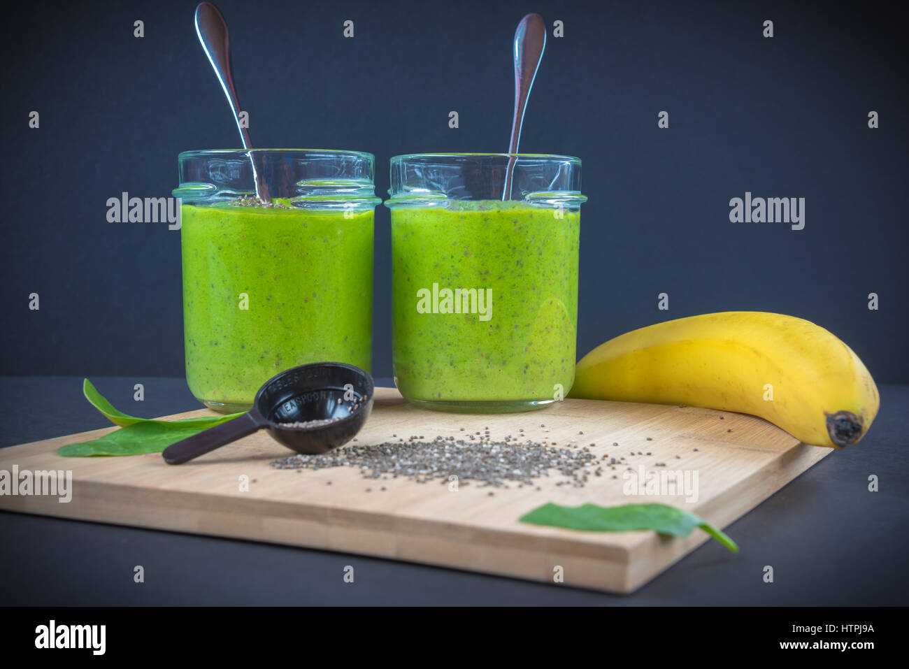 Épinards vert, semences chia, banane et de protéines en poudre dans deux bocaux smoothie sur la surface en bois de bambou et un arrière-plan sombre. parfait petit-déjeuner sain o Banque D'Images