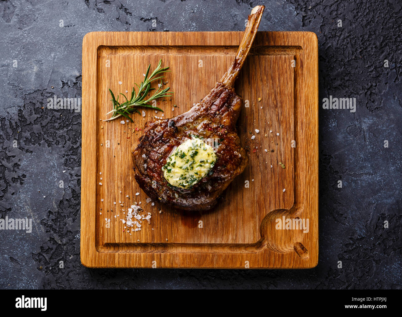 Le Steak grillé sur l'os de ris de veau de au beurre d'herbes sur une planche à découper sur fond sombre Banque D'Images