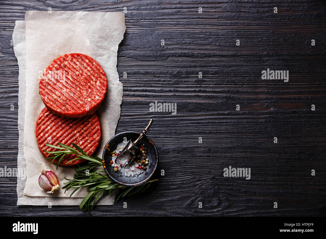 La viande de boeuf haché cru Burger steak escalopes et les assaisonnements sur fond de bois brûlé noir copy space Banque D'Images