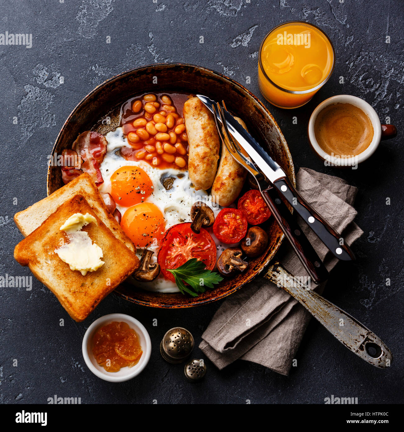 Le petit déjeuner anglais en plat de cuisson avec les œufs, saucisses, bacon, haricots, des toasts et du café à l'arrière-plan en pierre sombre Banque D'Images