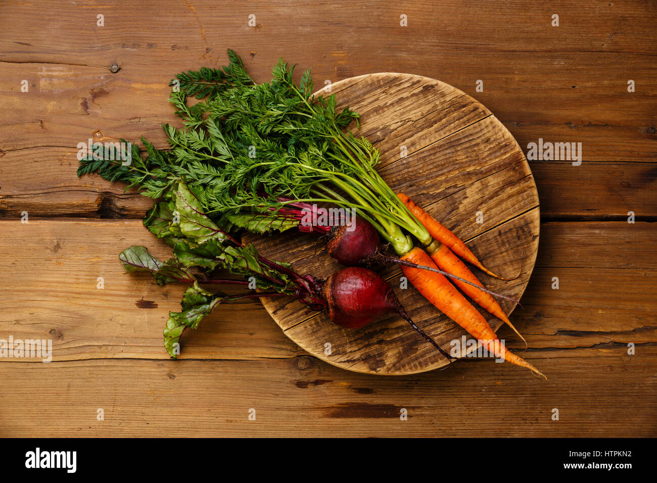 Légumes frais carottes et betteraves sur la planche à découper ronde sur fond de bois Banque D'Images