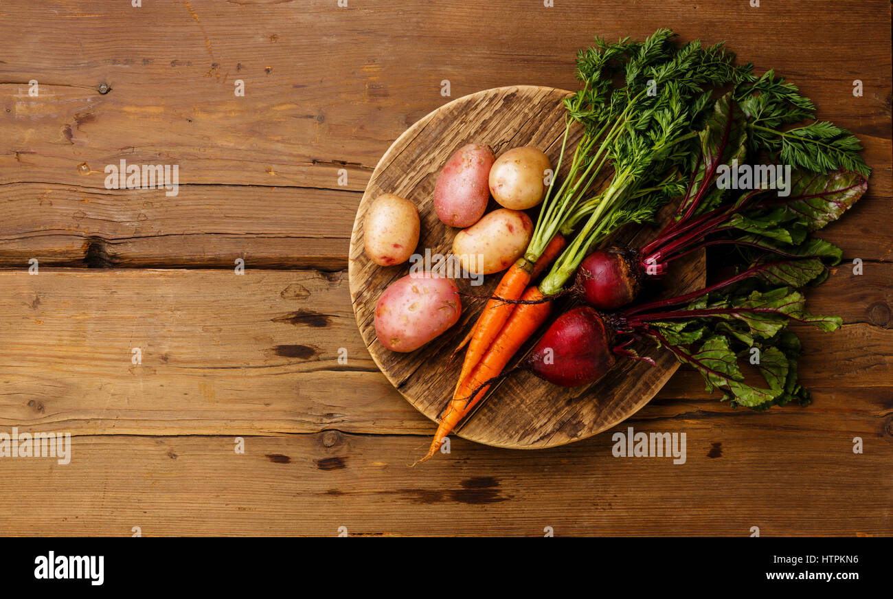 Légumes frais, carottes, pommes de terre et les betteraves sur la planche à découper ronde sur fond de bois copy space Banque D'Images