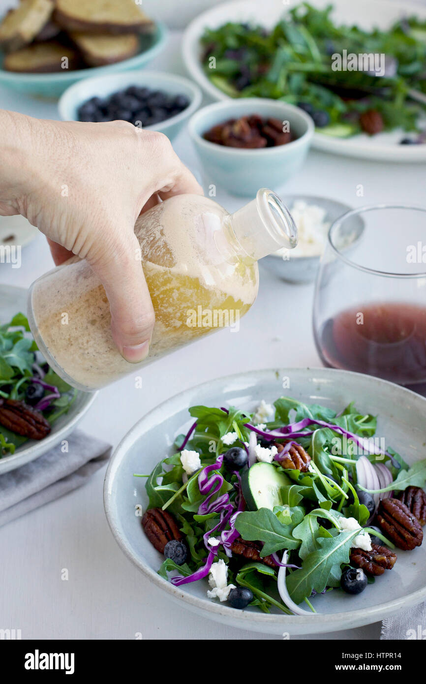 Verser la vinaigrette au feta grillée Sherry Noyer sur un pacanes épicées salade Feta servi avec du pain et du vin rouge. Photographié sur un bac blanc Banque D'Images