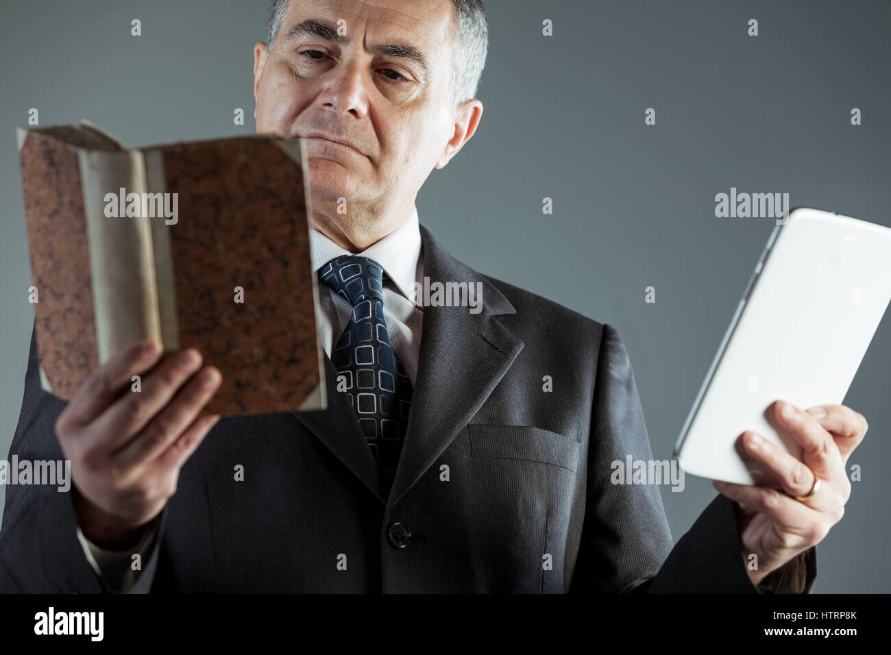 Businessman décider entre la lecture d'un livre relié traditionnel ou un e-livre sur sa tablette chaque tenu dans une main Banque D'Images