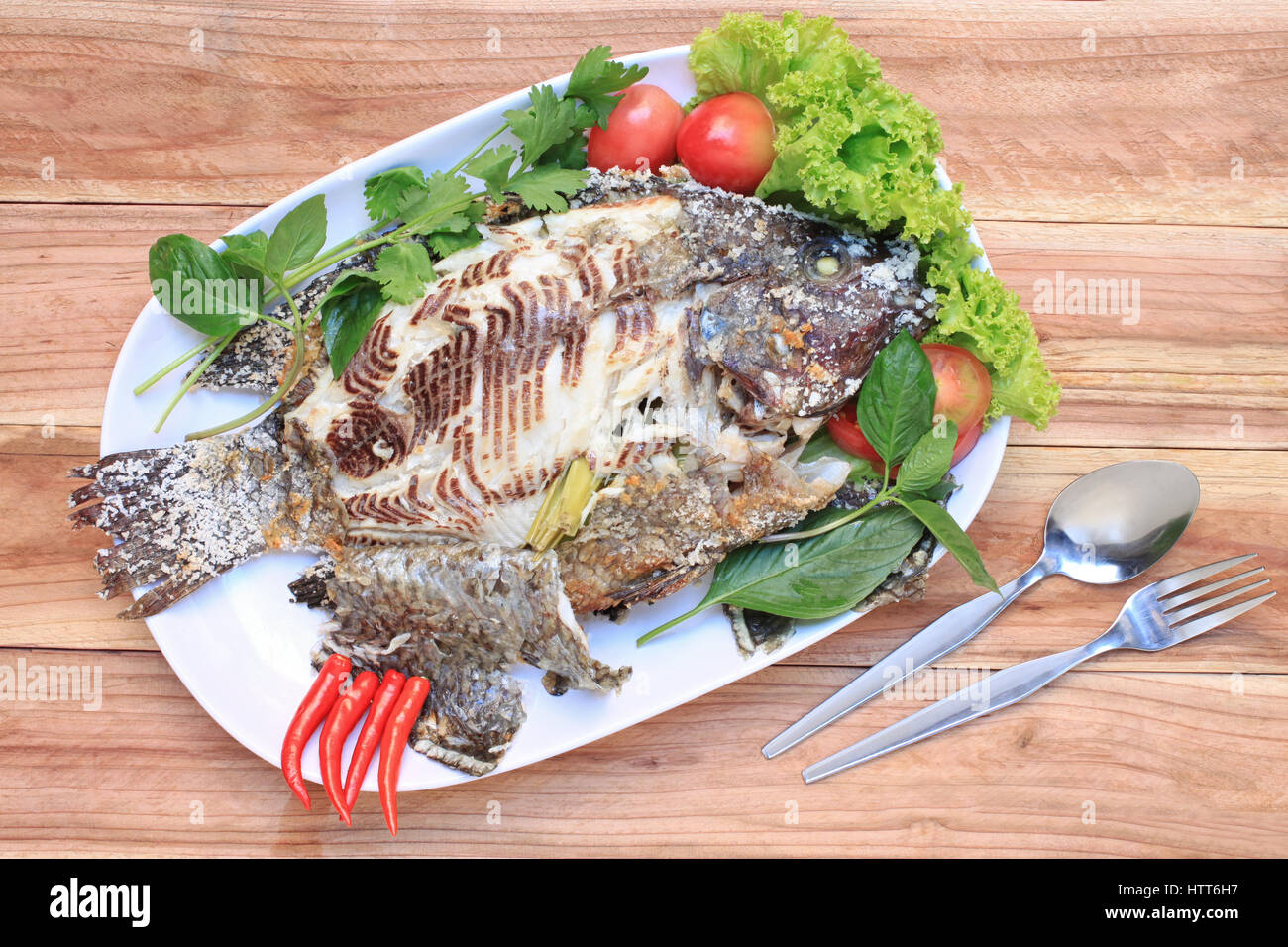 Le poisson Tilapia grillé au sel dans un plat blanc,Thai style aliments mis sur table en bois. Banque D'Images