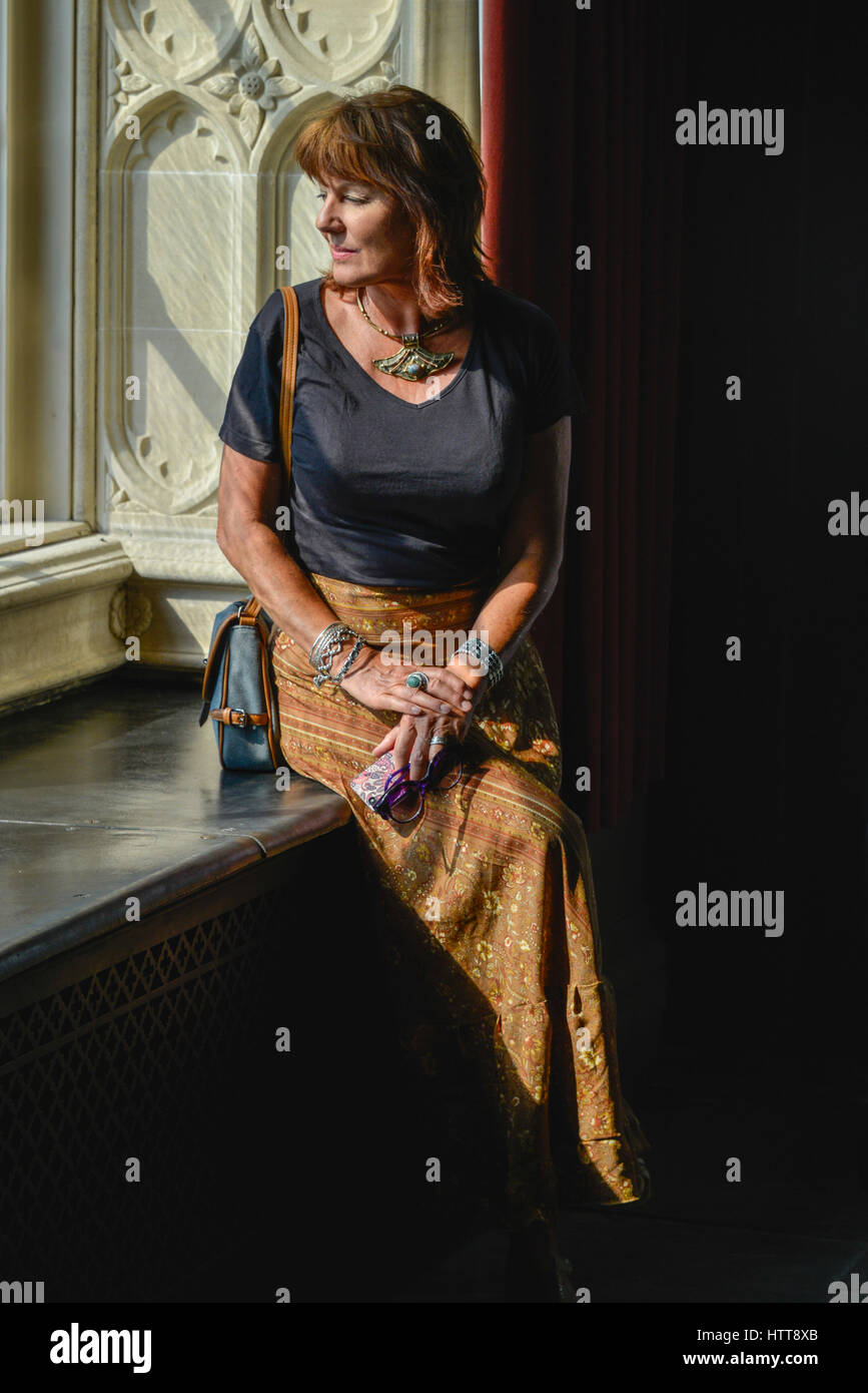 Femme à l'extérieur d'une fenêtre en baie, avec la lumière du soleil illuminant ses traits Banque D'Images