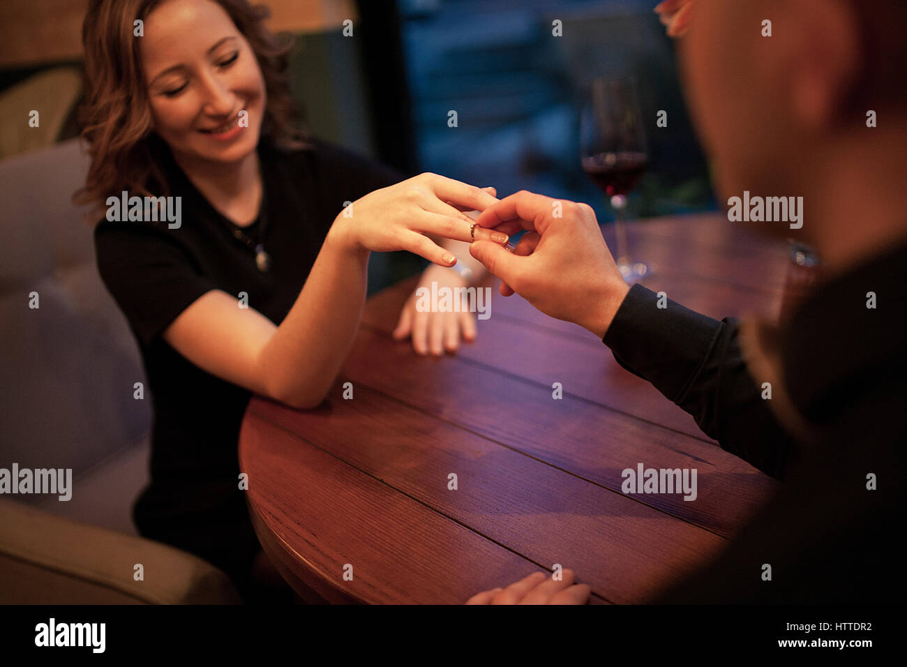 Jeune homme fait femme proposition de mariage et met une bague de fiançailles à son doigt. Ils sont assis à table à côté de verres de vin. Banque D'Images