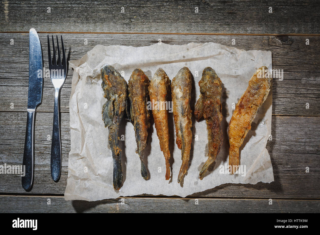 Le poisson séché avec fourchette et couteau sur la table. Salé poisson de rivière à sec sur un arrière-plan impressionnant en bois. Banque D'Images
