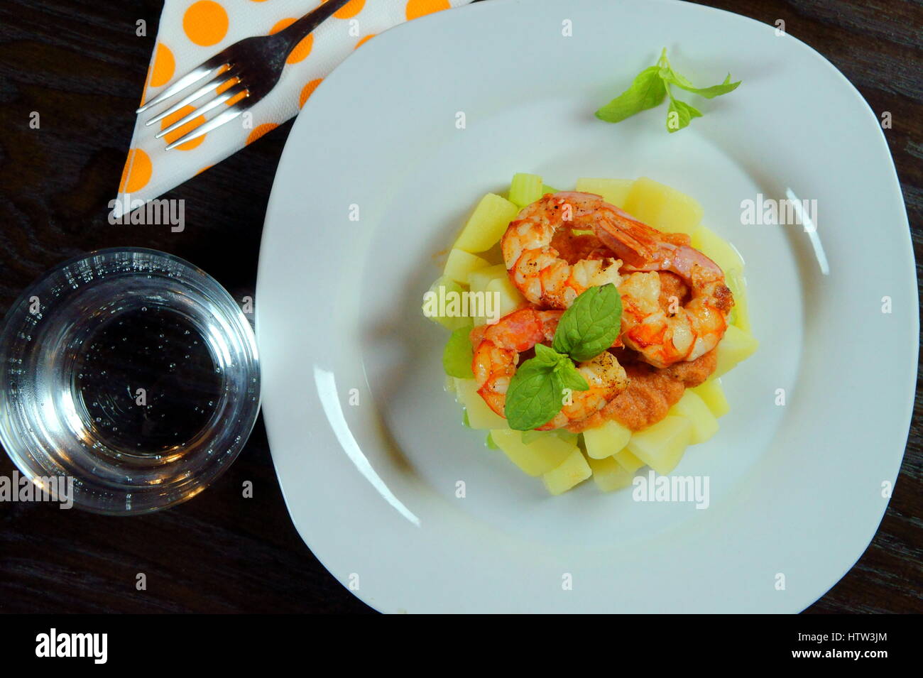 / Crevettes Salade de crevettes dans un plat blanc avec verre d'eau, serviette et fourchette sur table en bois foncé - Recette de fruits de mer avec des pommes de terre, le céleri, la sauce tomate, basilic Banque D'Images