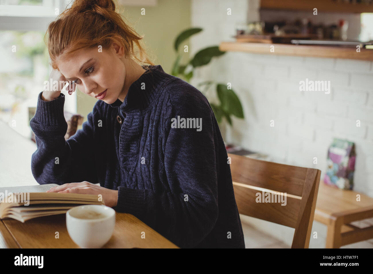 Femme assise à une table à manger et la lecture d'un livre Banque D'Images