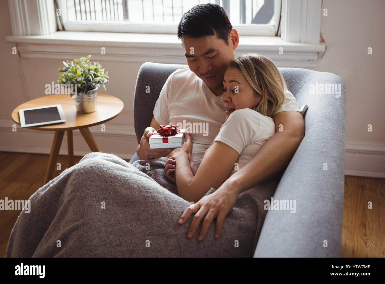 Man giving cadeau surprise à sa femme sur canapé Banque D'Images