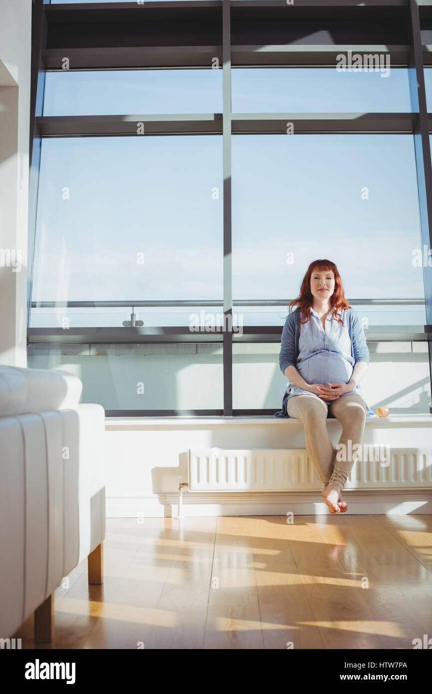 Femme enceinte assis près de fenêtre dans salle de séjour Banque D'Images