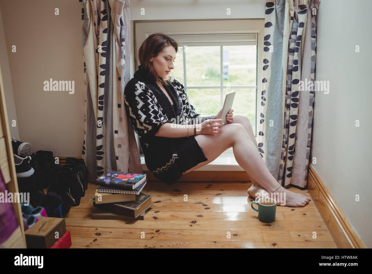 Femme assise au rebord de fenêtre et using digital tablet Banque D'Images