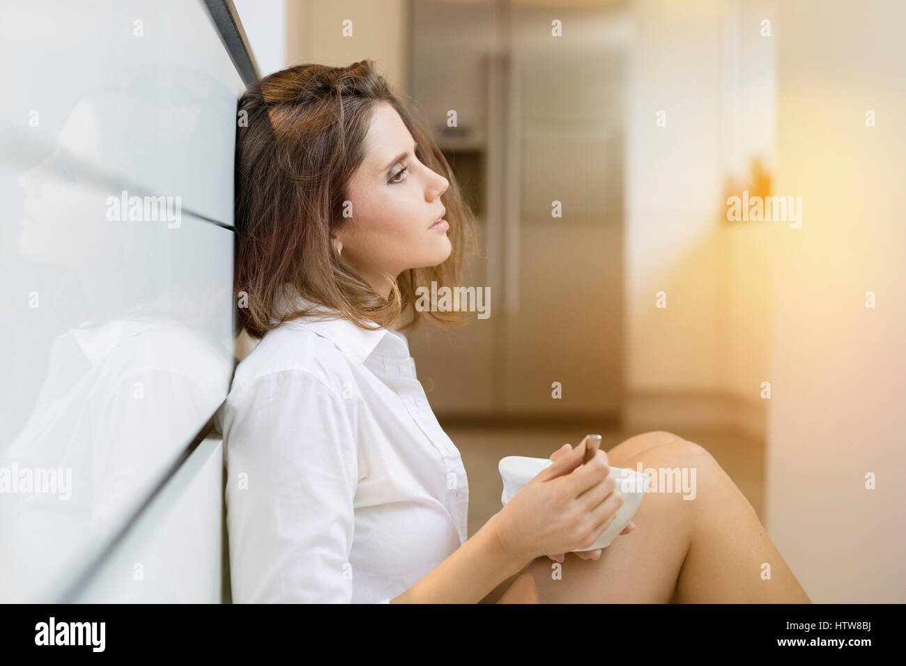 Jeune femme sur le plancher dans la cuisine manger du muesli Banque D'Images