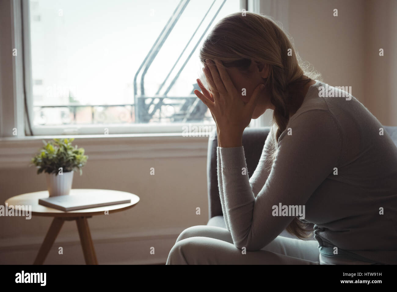 Tendu woman sitting on sofa in living room Banque D'Images