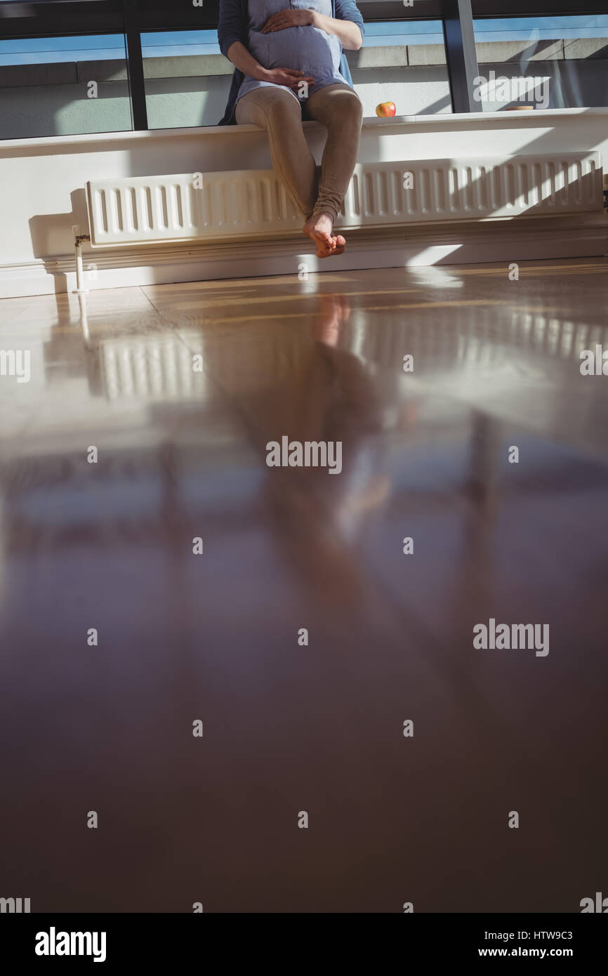 Femme enceinte assis près de fenêtre dans salle de séjour Banque D'Images