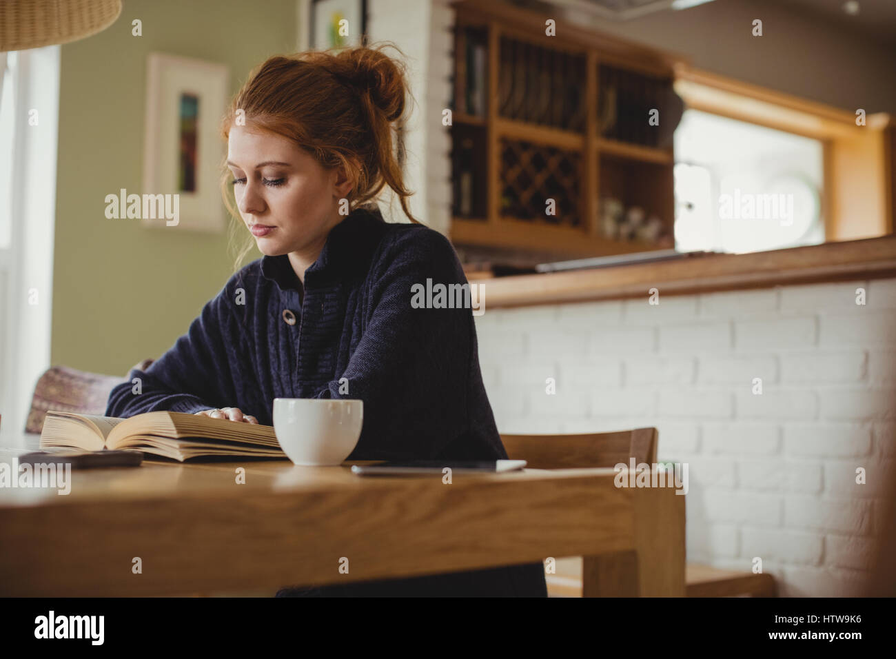 Femme assise à une table à manger et la lecture d'un livre Banque D'Images