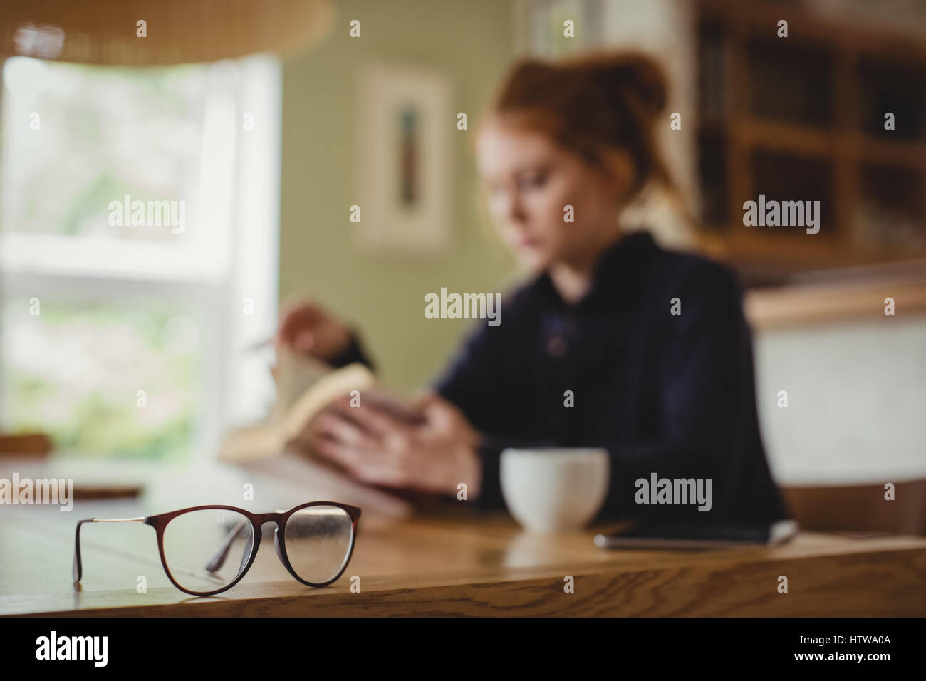 Femme assise à une table à manger et la lecture d'un livre Banque D'Images